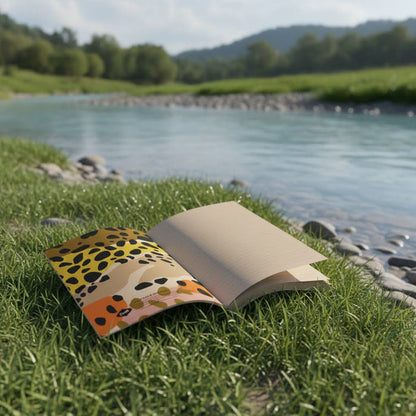 Forager Provisions LTD Denik trout kraft layflat notebook open on grassy riverbank with a scenic nature background.