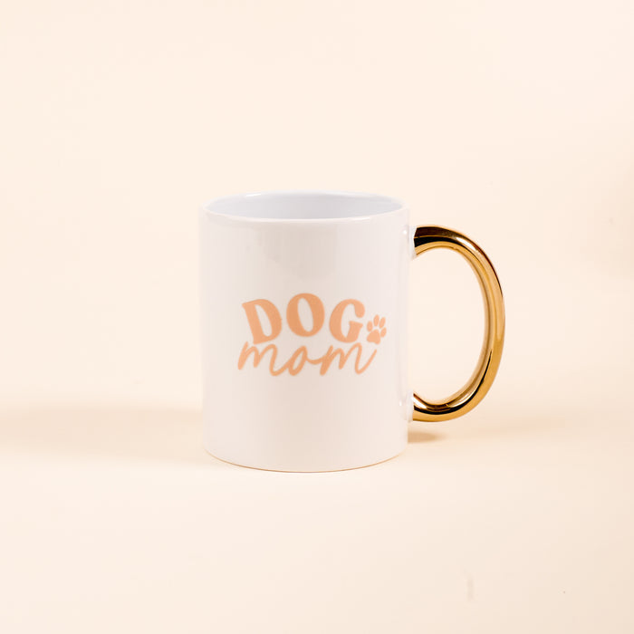 Enjoy your favorite drinks with The Darling Effect’s Dog Mom 11 oz Cozy Cute Ceramic Mug, featuring peach “Dog Mom” text and a paw print on cream ceramic, accented by a golden handle.