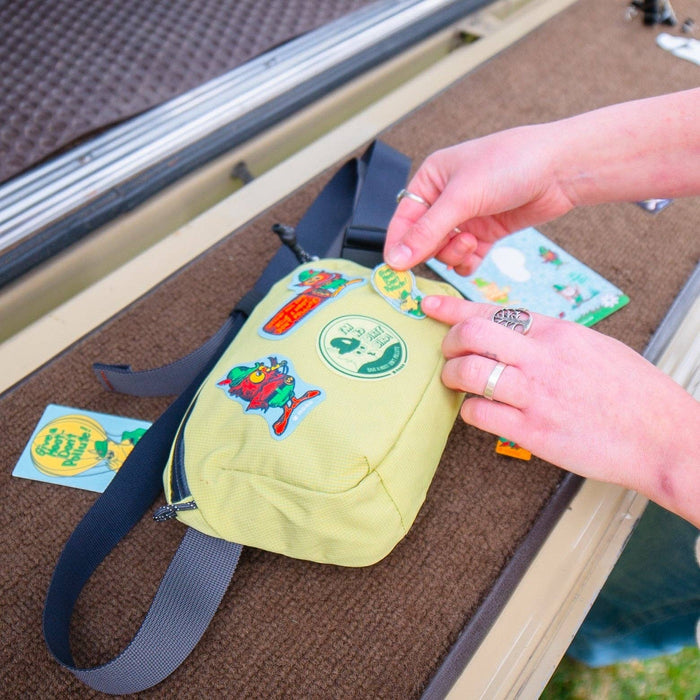 Applying NoSo Patches Don’t Pollute Woodsy Owl patch to yellow bag, extra eco-friendly repair patches displayed close by.