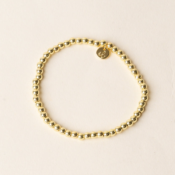 The Ella Beaded Bracelet by the-darling-effect features gold beads and a small round charm inscribed with the letter L—ideal for fans of customizable jewelry.