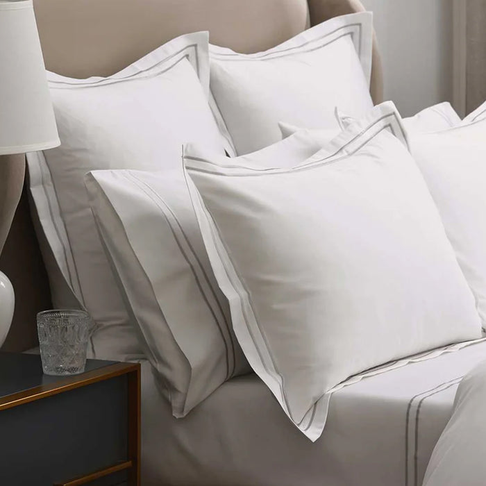 Empire Silver Pillowcases on a bed with a side table and lamp in the background