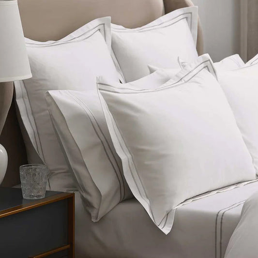Empire Silver Pillowcases on a bed with a side table and lamp in the background