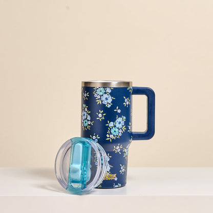 The-darling-effect Endless Daydream Navy 20 oz Lifestyle Flip Straw Tumbler stands upright with its clear lid featuring a blue sliding cover resting beside it. The insulated stainless steel tumbler has light blue floral patterns.
