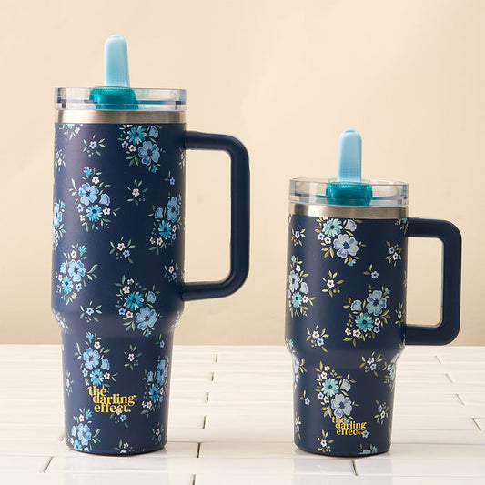 Two navy blue "Endless Daydream" 40 oz Lifestyle Flip Straw Tumblers by the-darling-effect, featuring blue floral patterns, large handles, clear lids, and blue silicone straws, are set on white tiles with a beige background.