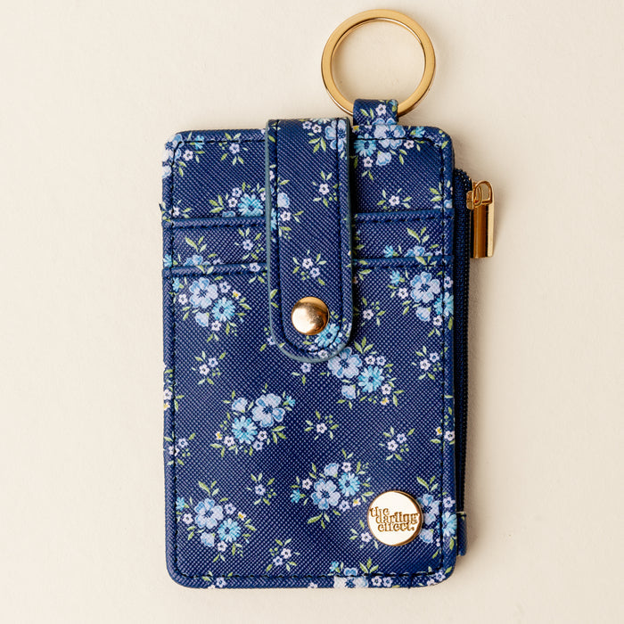 The Endless Daydream Navy Keychain Wallet by the-darling-effect features a navy floral design, zippered coin holder, gold snap button, keyring, and a round gold emblem in the corner.