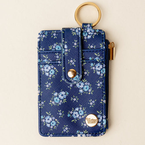 The Endless Daydream Navy Keychain Wallet by the-darling-effect features a navy floral design, zippered coin holder, gold snap button, keyring, and a round gold emblem in the corner.