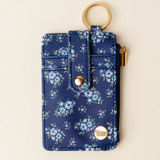 The Endless Daydream Navy Keychain Wallet by the-darling-effect features a navy floral design, zippered coin holder, gold snap button, keyring, and a round gold emblem in the corner.