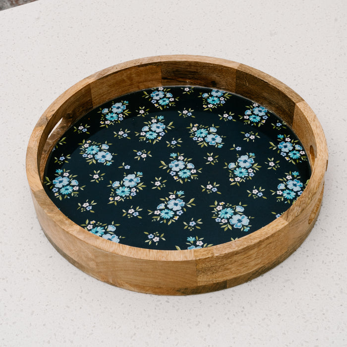 The Endless Daydream Navy Large Round Wood Enamel Tray by the-darling-effect features a dark base with blue and white floral details, adding a charming touch to any light-colored surface.