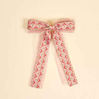 The Darling Effect Everbloom Dusty Rose Lovely Layered Hair Bow features a pink floral print with red and green botanicals, sheer organza edges, and long trailing ribbons—a charming hair accessory for any collection.