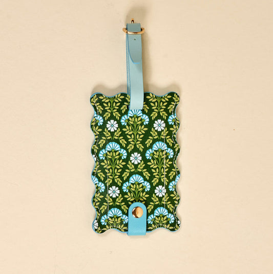 The Darling Effect Everbloom Forest Green Jetsetter Luggage Tag features a scalloped edge, blue strap with gold buckle, green background with blue and white floral pattern, plus a privacy flap for secure travel.