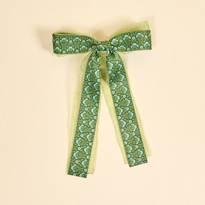 The Darling Effect’s Everbloom Forest Green Lovely Layered Hair Bow features sheer light green ribbon, a dark green overlay, and blue floral accents—an enchanting addition to any hair accessories collection.