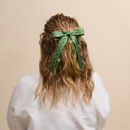A woman’s wavy blonde hair is styled with The Darling Effect’s Everbloom Forest Green Lovely Layered Hair Bow—an elegant, floral-inspired accessory choice.