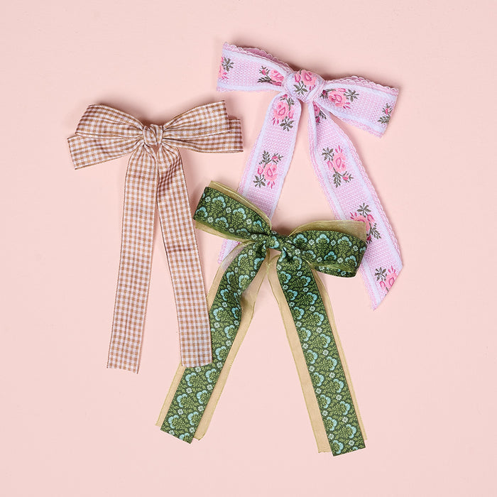 The Darling Effect’s Everbloom Forest Green Lovely Layered Hair Bow is a charming hair accessory, beautifully displayed on a pink background.
