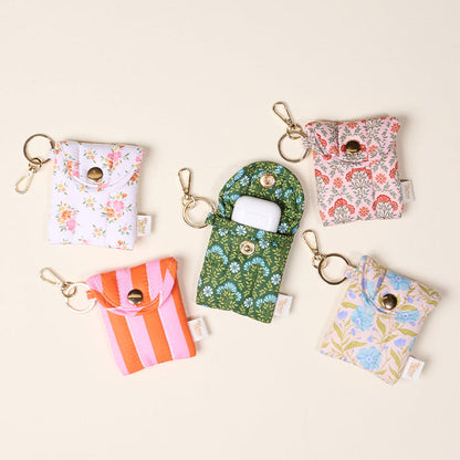 Five small, colorful Puffy Earbud Cases from The Darling Effect are arranged in a circle, each with a keychain clip. In the center, the Everbloom Forest Green Puffy Earbud Case is open to reveal a white wireless earbuds case inside.