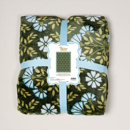 The Darling Effect's Everbloom Forest Green Snuggle Up Plush Blanket features white and blue floral patterns, neatly folded with a light blue ribbon and label—perfect for adding cozy comfort to any space.