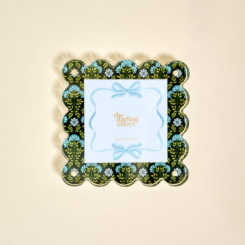 The Everbloom Forest Green Square Scalloped Acrylic Picture Frame by The Darling Effect features a black background with a blue, green, and white floral pattern and holds a card reading "the darling effect" in gold text.