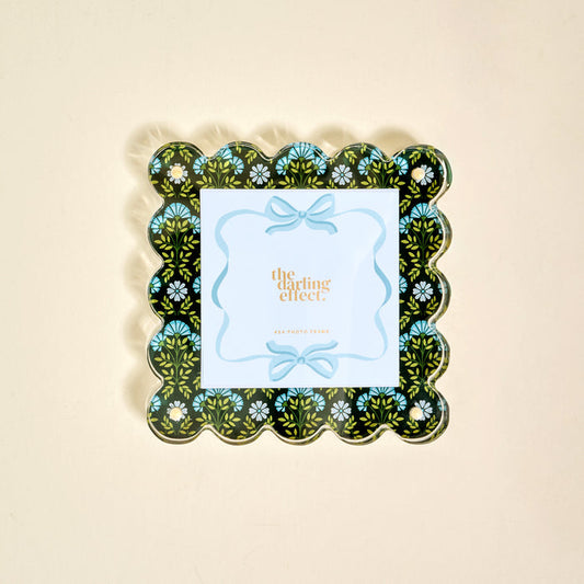 The Everbloom Forest Green Square Scalloped Acrylic Picture Frame by The Darling Effect features a black background with a blue, green, and white floral pattern and holds a card reading "the darling effect" in gold text.