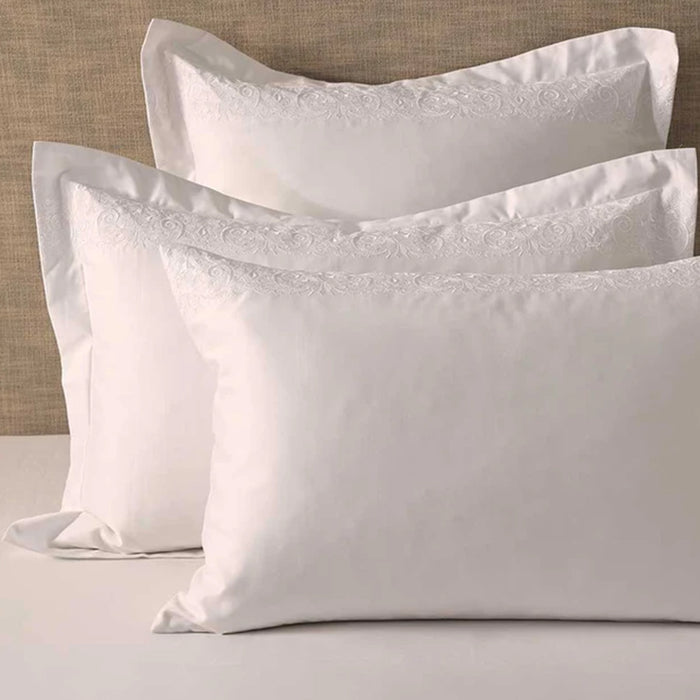Fion White Pillowcases on a bed against a beige wall.