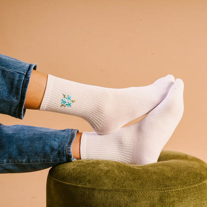 The Darling Effect Floral Blue Embroidered Crew Socks styled with blue jeans, resting on a green pouf.