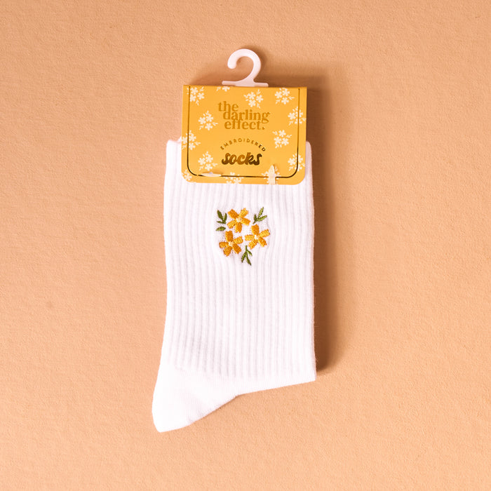 The Darling Effect Floral Yellow Embroidered Crew Socks, featuring playful yellow flower designs, are shown on a hanger with a branded tag. Available in women’s sizes 5–10.