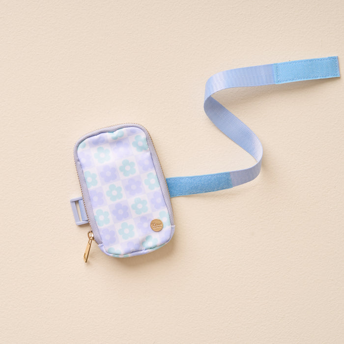 The Darling Effect's Flower Check Blue Tumbler Fanny Pack features a pastel blue and white floral pattern, gold zipper, adjustable light blue strap, and is water resistant. Shown on a light beige background.
