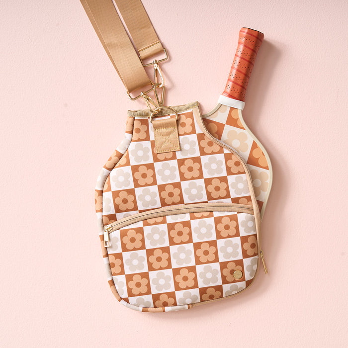The Darling Effect's Flower Check Brown Pickleball Paddle Case features a beige and tan floral design, a front zipper pocket, and holds a matching retro flower paddle—both seen against a pale pink background.
