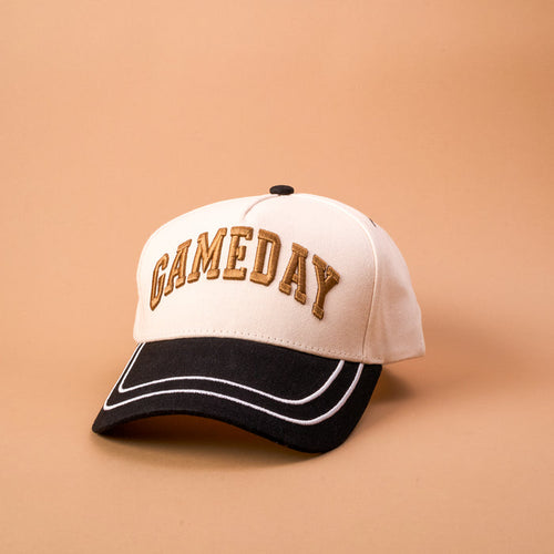 The Darling Effect's Gameday Classic Canvas Hat is a beige and black baseball cap with "GAMEDAY" embroidered in gold on the front. Featuring a relaxed fit, this classic hat is shown against a light tan background.