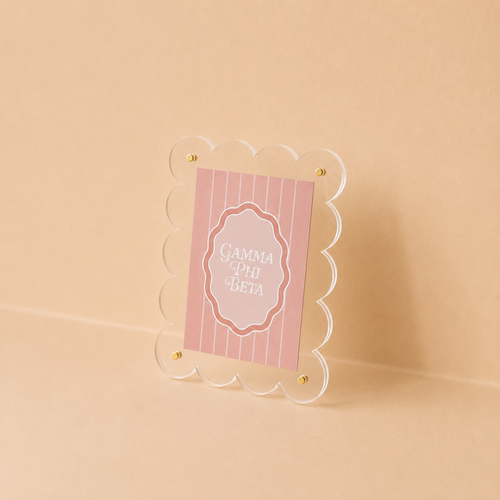 The Darling Effect’s Gamma Phi Beta Mini Acrylic Picture Frame Magnet features a scalloped clear frame displaying a pink, vertically striped card with white “Gamma Phi Beta” text, ideal for mini or polaroid photos.