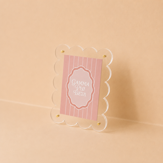 The Darling Effect’s Gamma Phi Beta Mini Acrylic Picture Frame Magnet features a scalloped clear frame displaying a pink, vertically striped card with white “Gamma Phi Beta” text, ideal for mini or polaroid photos.