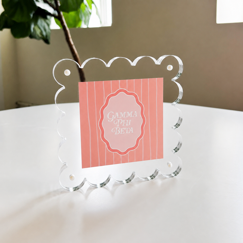 The Darling Effect’s Gamma Phi Beta Square Scalloped Acrylic Frame showcases a pink, vertically striped “Gamma Phi Beta” card in white script—a chic, modern accent for your space.