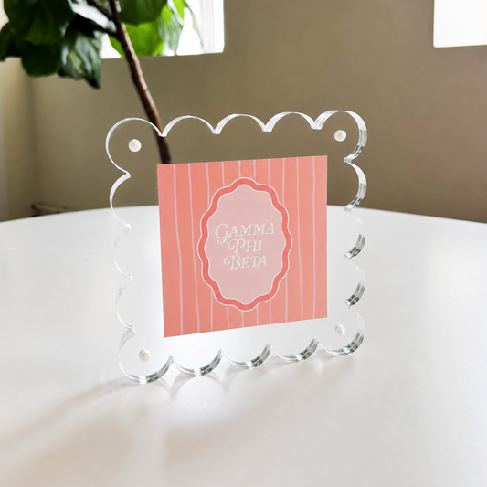 The Darling Effect’s Gamma Phi Beta Square Scalloped Acrylic Frame showcases a pink, vertically striped “Gamma Phi Beta” card in white script—a chic, modern accent for your space.