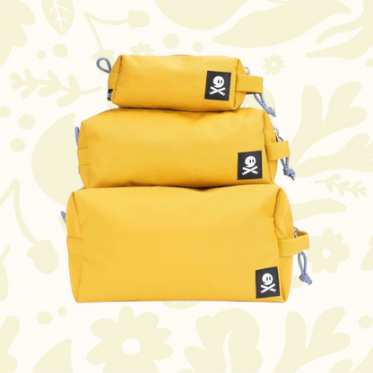 Three Ghost Outdoors ochre yellow Dopp Kits stacked on vibrant floral background, stylish travel toiletry bags display.