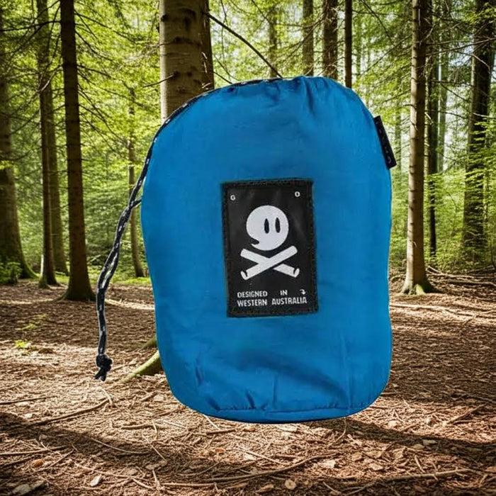 Forager Provisions LTD Ghost Outdoors peacock blue packable travel hammock in its compact storage bag in a forest.