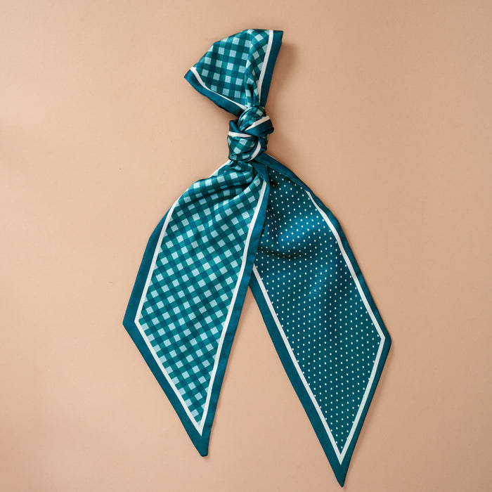 The Darling Effect's Gingham Green Twirl & Tie Scarf Accessory features a teal satin scarf with one side in a checkered pattern and the other in polka dots, stylishly tied in a loose knot and displayed against a light beige background—making it perfect for limitless styling possibilities.