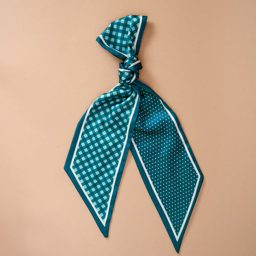 The Darling Effect's Gingham Green Twirl & Tie Scarf Accessory features a teal satin scarf with one side in a checkered pattern and the other in polka dots, stylishly tied in a loose knot and displayed against a light beige background—making it perfect for limitless styling possibilities.