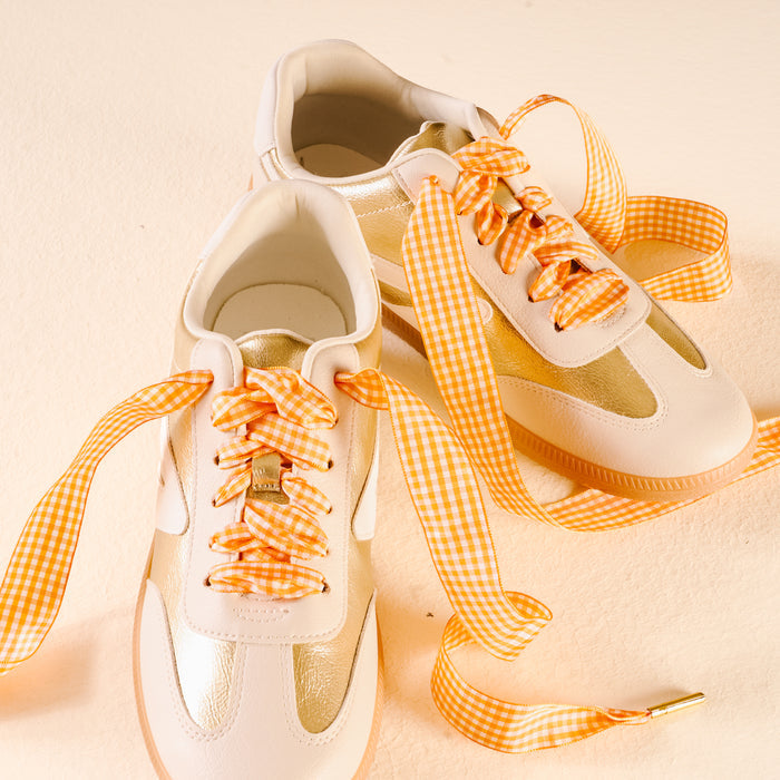 Close-up of two white and gold sneakers with The Darling Effect’s Gingham Orange Step It Up Shoelaces featuring a bright orange and white gingham pattern.