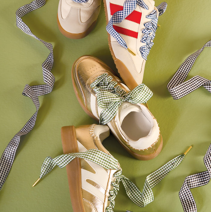 Three pairs of retro-style sneakers with gum soles on a green background, each featuring oversized, durable The Darling Effect Gingham Purple Step It Up Shoelaces in checkered patterns, including standout bold red stripes.
