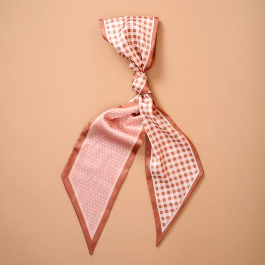 The Darling Effect's Gingham Tan Twirl & Tie Scarf Accessory is showcased on a peach-colored background, featuring one side with gingham checks and the other with playful polka dots—ideal for versatile styling when tied in a loose knot.