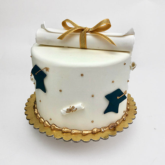 The Graduation Cake is iced in white buttercream, this cake features fondant grad caps along the sides and a fondant scroll with a gold ribbon on top.
