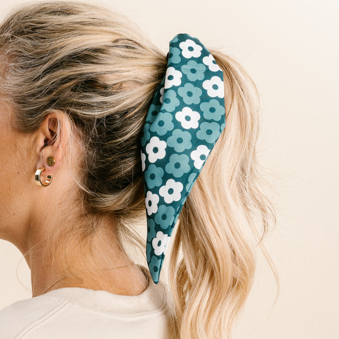 A woman with blonde hair in a ponytail wears The Darling Effect's Green Game Day Hair Scarf with Scrunchie. She has gold earrings and is pictured from the side against a neutral background, showing her team spirit.