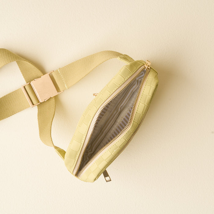 The Darling Effect’s Green Urban Check Belt Bag, featuring a light green checkered pattern, open zipper, and gold buckle, is displayed from above on a cream background—making it a trendy accessory for any outfit.