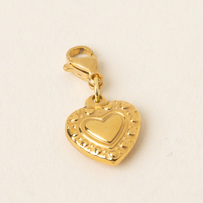 The-darling-effect Heart Jewelry Charm Gold features a small gold heart with a raised center design and lobster clasp, ideal for charm bars or mixing with other unique jewelry charms. Displayed on a light background.