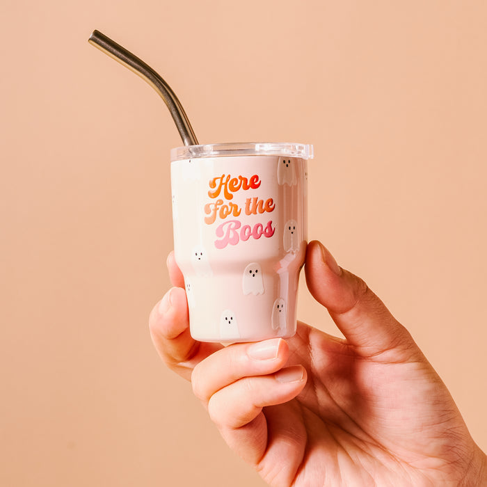 A hand holds The Darling Effect's "Here for the Boos" 2 oz Tiny Tumbler, featuring a pale pink ghost pattern and a metal straw.