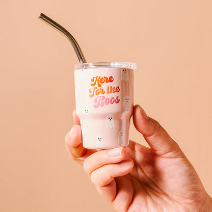 A hand holds The Darling Effect's "Here for the Boos" 2 oz Tiny Tumbler, featuring a pale pink ghost pattern and a metal straw.