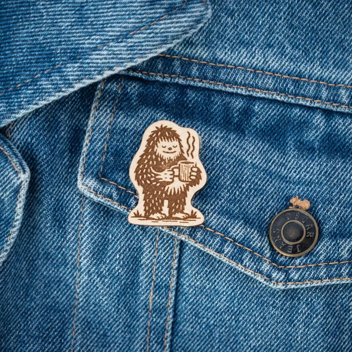 Forager Provisions LTD Hey Bear Outdoors wooden Bigfoot pin badge attached to a blue denim jacket pocket.