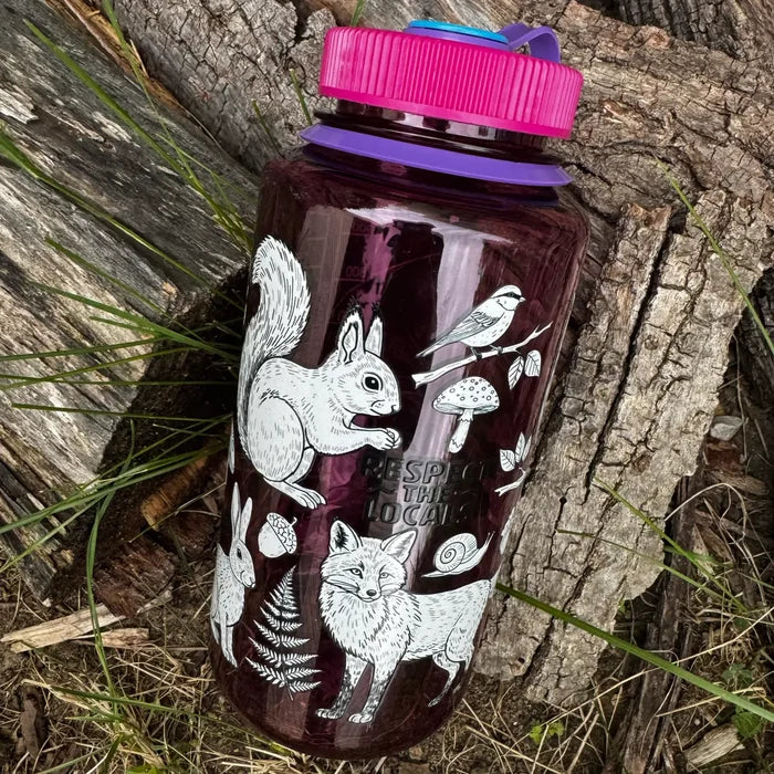 Hey Bear Outdoors “Respect The Locals” 32oz Nalgene bottle on grass and logs, ideal for outdoor hydration and adventure.