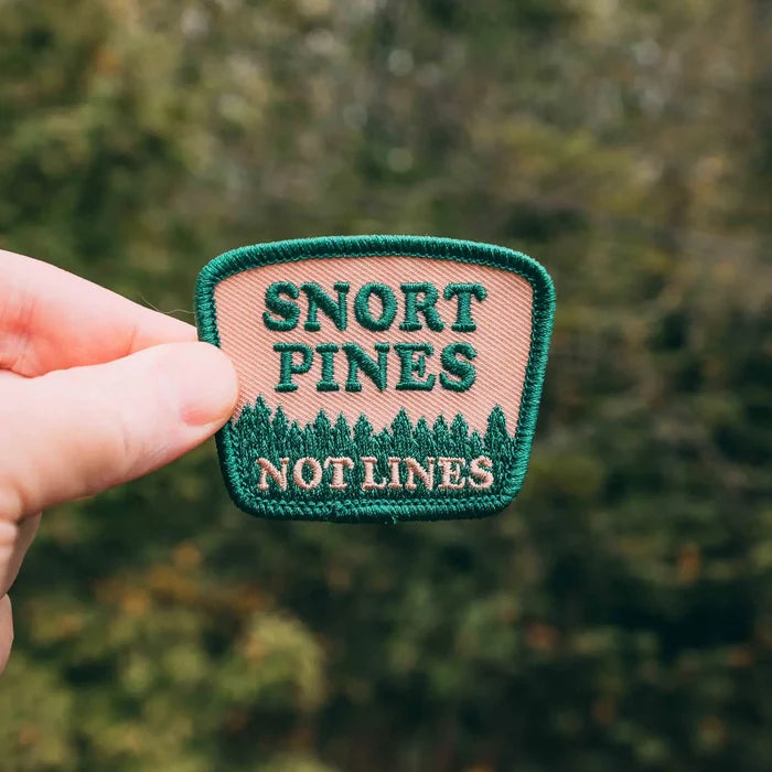 Hand holding Hey Bear Outdoors Snort Pines Not Lines embroidered hiker patch, pine tree design, outdoor hiking gear accessory.
