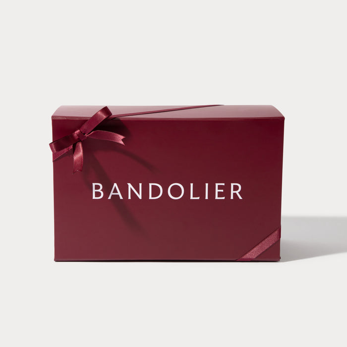 A burgundy Bandolier gift box, tied with a satin ribbon forming a bow on the left and wrapping around the lower right.