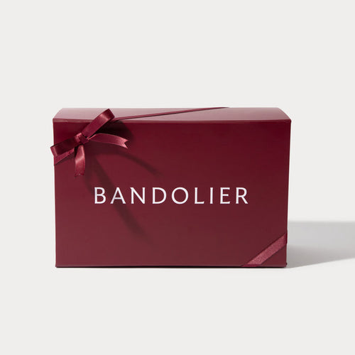 A burgundy Bandolier gift box, tied with a satin ribbon forming a bow on the left and wrapping around the lower right.