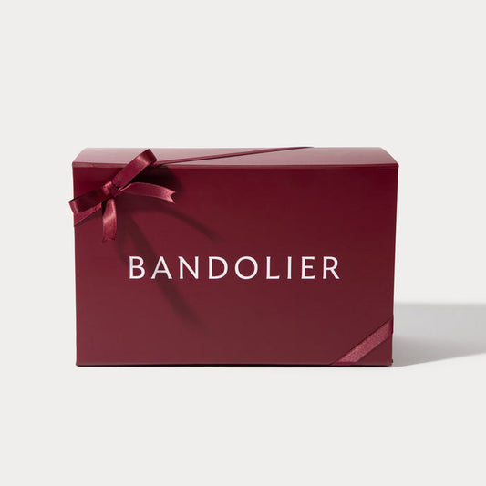 A burgundy Bandolier gift box, tied with a satin ribbon forming a bow on the left and wrapping around the lower right.